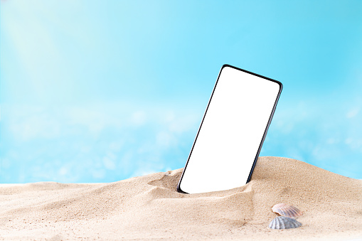 Smartphone with white screen on sandy beach, copy space