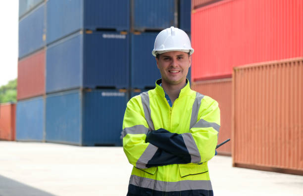 istock Worker wearing white hardhat cross his arms looking at camera with cargo containers background. 1407127446