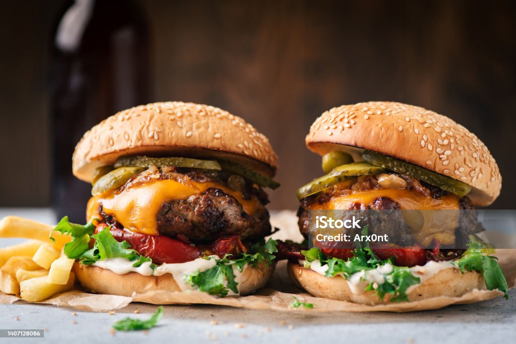 Two juicy craft cheeseburgers with roasted bell pepper and pickles Two juicy craft cheeseburgers with roasted bell pepper and pickles served with french fries on parchment paper, wooden background Burger Stock Photo