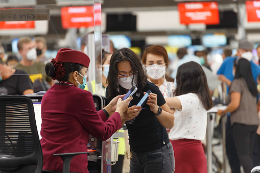 Bangkok, Thailand - July 6, 2022 : asian passenger using smart phone to check in at airline counter in suvarnabhumi airport, Thailand. Travel and transportation concept.