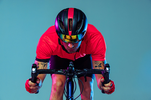 Champion. Studio shot of professional cyclist in red sports uniform, goggles and a helmet on a blue background. Concept of active life, rest, travel, energy, sport. Copy space for ad