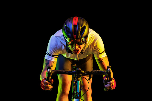 Racer. Portrait of professional male cyclist in sports uniform, goggles and helmet on dark background in yellow neon light. Concept of active life, rest, travel, energy, sport. Copy space for ad. Front view