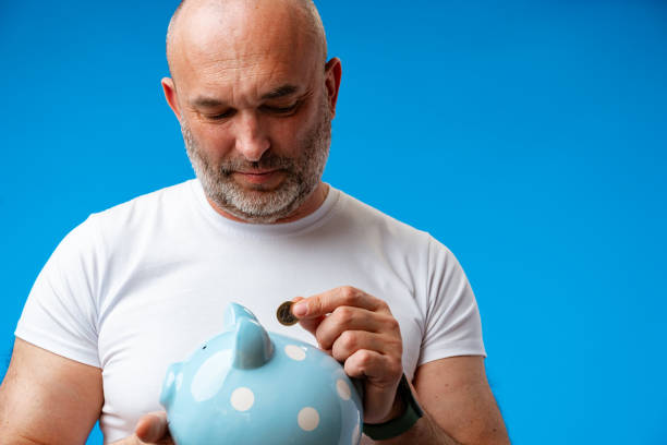 istock Middle-aged man holding piggy bank against blue background 1407132155