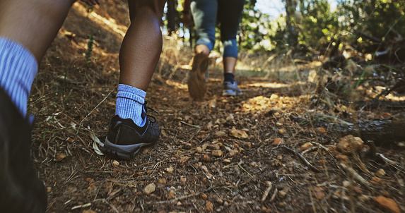 Closeup of hikers walking up a trail in the forest outdoors with copyspace. Feet of two adventurous people from the back exploring nature as a recreational hobby. Tourists hiking a scenic path uphill