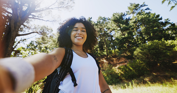 Portrait of a hiker taking selfies and exploring a trail in nature on a sunny day with copy space. Smiling black woman with curly afro hair enjoying the fresh air during a solo trek in the wilderness