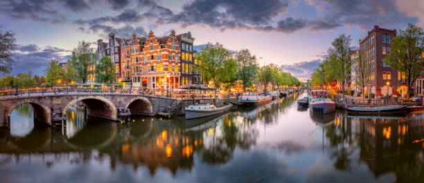 amsterdam. panoramablick auf die innenstadt von amsterdam. traditionelle häuser und brücken von amsterdam. eine blaue abendzeit und die ruhige reflexion von lichtern im wasser. langzeitbelichtung. - amstel river amsterdam architecture bridge stock-fotos und bilder