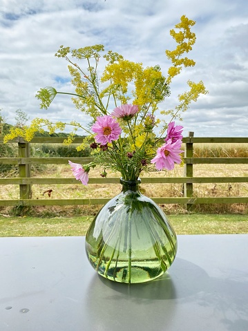 Vase of freshly picked wildflowers and herbs in a garden with field view