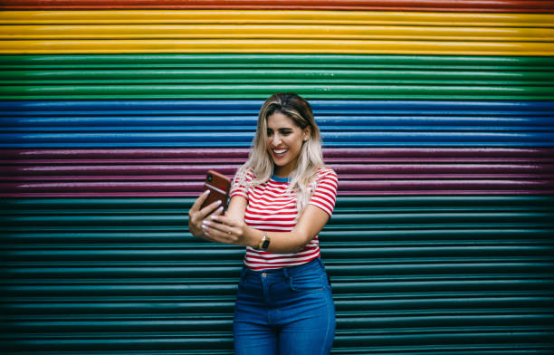cheerful female vlogger smiling at smartphone camera posing at colorful promotional background, happy hispanic hipster girl 20 years old rejoicing near copy space publicity while clicking selfie - women spain 20 25 years adult imagens e fotografias de stock