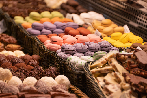 Hand picking up a chocolate macaron from a plate full of various flavors on wooden table and dark background. Front view.