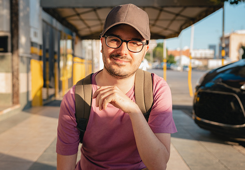 Young man with glasses and a cap looking at camera outside