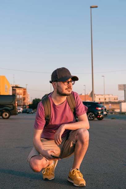 istock Casual man squatting is wearing a cap and a backpack on the street 1407149174