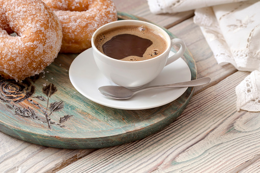 Brewed coffee in a white cup with delicious donuts on a wooden table close-up