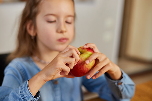 Cute little girl eat red apple at home at kitchen interior, yummy, happy child, Healthy nutrition diet vegetarian food lifestyle.