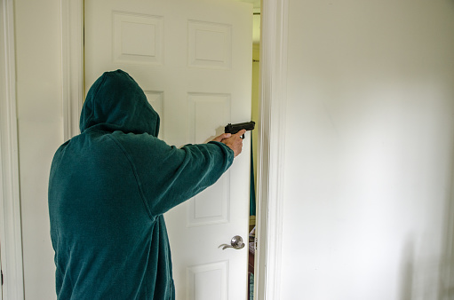 Armed man opening bedroom door inside house