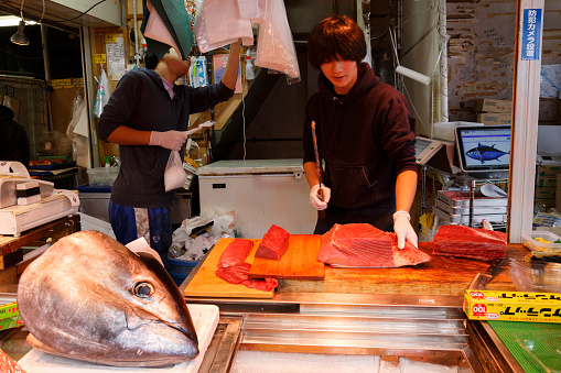 Tsukiji, Tokyo, Japan - June 30, 2022 : Japanese fishmonger slicing yellow fin tuna to sell in the stall at Tsukiji Fish Market in Tokyo, Japan. Selective focus and film style photo.
