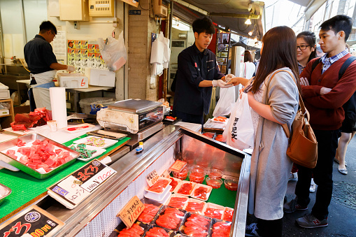 Tsukiji, Tokyo, Japan - June 30, 2022 : Japanese fishmonger sell fresh slicing sashimi yellow fin tuna meat to customer at seafood stall in Tsukiji Fish Market, Tokyo, Japan.