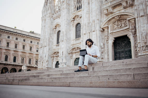 Businessman sitting on the steps in front of the Duomo working on digital tablet and having a call