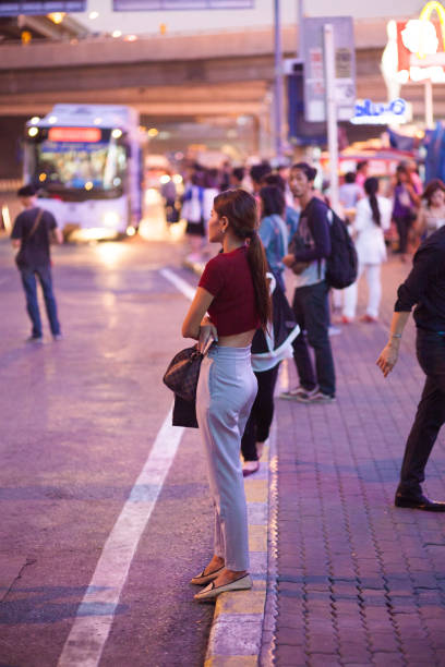 Thai people and commuters are standing at bus stop in night. Scene is at bus stop and mini van stop in Bangkok Rangsit at Future Park. In foreground a woman is standing. In background a bus is approaching