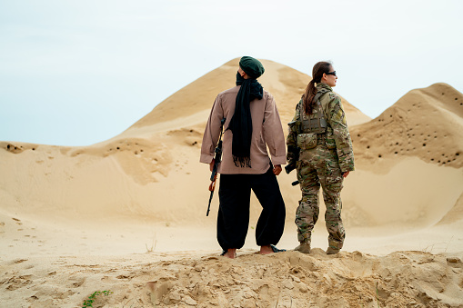 Man with veil stay with military or soldier woman in desert and look around during prepare for battle to enemy.