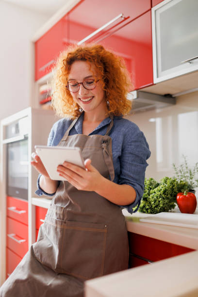 istock Young woman using her digital tablet while cooking at home 1407159156