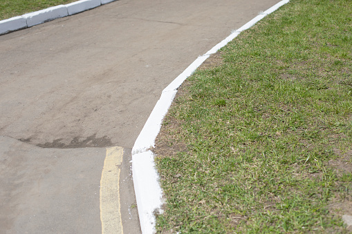 White curb on road. Landscaping in park. Painted curb.