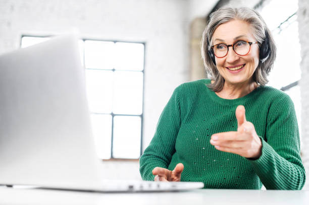 istock Beautiful senior woman wearing headset using laptop 1407163051