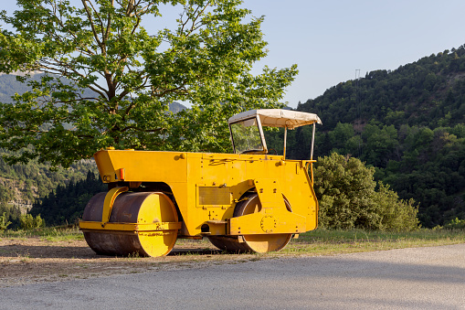 A soil compactor for road asphalting is parked near the road in the mountains on a sunny, summer day