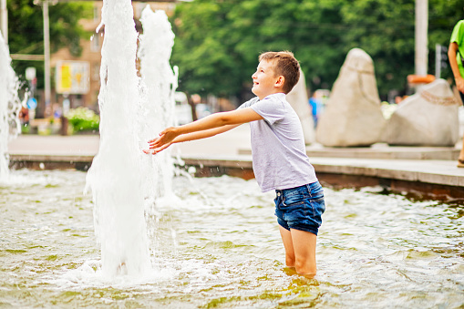 A boy having fun in water fountains. Child playing with a city fountain on hot summer day. Summer weather. Active leisure, lifestyle and vacation.