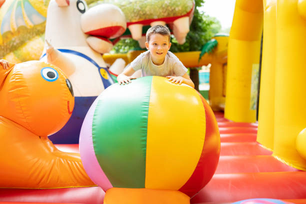 szczęśliwy chłopiec świetnie się bawiący na kolorowym nadmuchanym zamku. kolorowy plac zabaw. centrum aktywności i zabaw dla dzieci - inflatable slide sliding child zdjęcia i obrazy z banku zdjęć