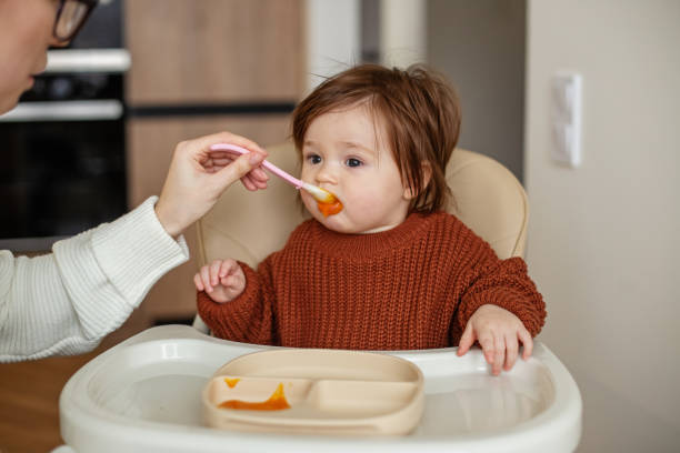 comida deliciosa y saludable para los niños. la niña pequeña come puré de fruta para bebés de una cuchara. - baby carrot fotografías e imágenes de stock
