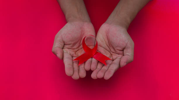 istock Hand holding a Red AIDS Ribbon with copy space for text isolated on red background 1407165983