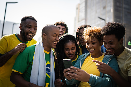 Brazilian fans watching soccer game using mobile phone outdoors