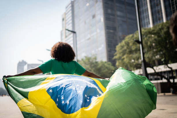 aficionado brasileño caminando y sosteniendo una bandera brasileña en la ciudad - brasilero fotografías e imágenes de stock