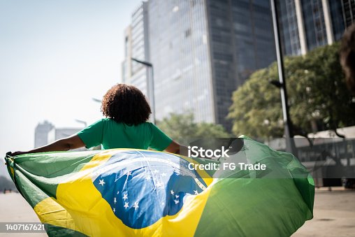 istock Brazilian fan walking and holding a brazilian flag on the city 1407167621