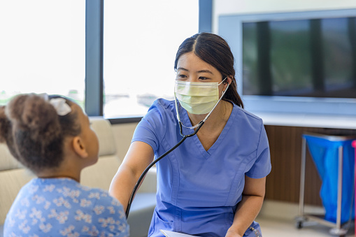The nurse smiles through her protective face mask at her young patient.
