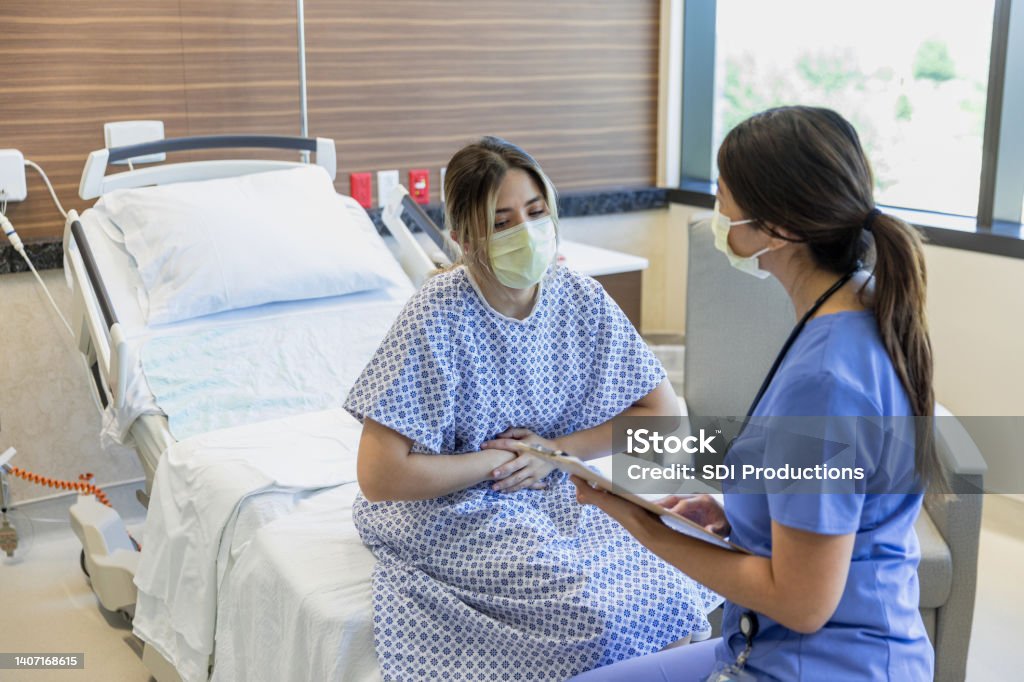 Female patient grabs her stomach The female patient grabs her stomach in pain as she sits with the nurse to review symptoms. Miscarriage Stock Photo