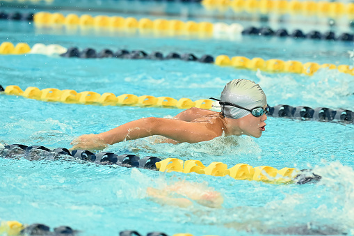 A senior African-American woman, in her 70s, swimming laps. She is in a lane, between two lane markers, swimming freestyle.