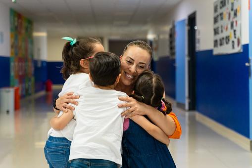 Happy students embracing teacher in classroom