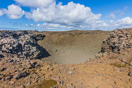 Crater of a volcano in the day with sunshine and clouds in the sky. Landscape on Iceland of Reykjanes Peninsula. Brown and gray lava rocks and along the rim of the crater