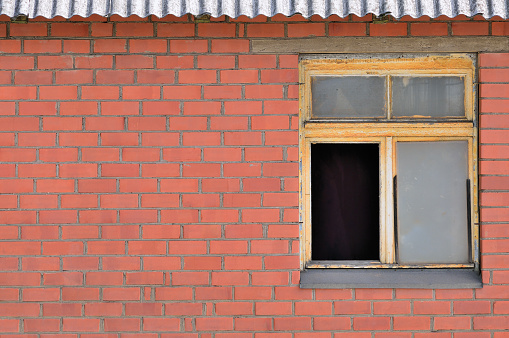 Old aged shed broken window glass, red bricks hut wall background, weathered grungy rusty dirty damaged wooden frame, textured large detailed horizontal shack backdrop, blank empty copy space closeup, grunge rust pattern, crime and poverty broken windows theory concept metaphor, slated grey roof