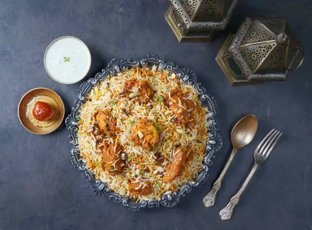 Indian spicy Chicken Tikka Biryani with raita and gulab jamun Served in a dish top view on grey background