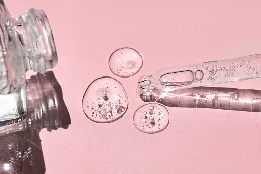 Close up of glass bottle and pipette with fluid collagen and hyaluronic acid, hydration skin with shadows on pastel pink background on sunlight. Cosmetology, dermatology concept.
