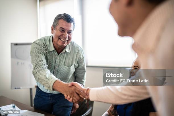 Coworkers Greeting And Doing A Handshake At Work Stock Photo - Download Image Now - Agreement, Senior Adult, Latin American and Hispanic Ethnicity