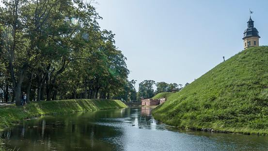 Nesvizh, Belarus - June 19, 2022: Fortress moat with water reflecting trees and castle walls. Bridge over the moat. Heritage concepts.
