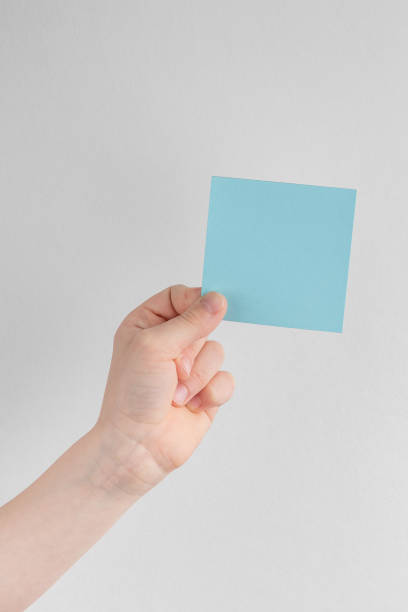 istock child hand holding a square blue blank reminder or paper notes above a white and gray background, copy space 1407184293