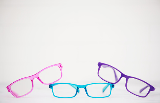 Three pairs of brightly colored modern eyeglasses shot in a bright setting with space for copy