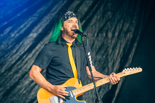 Male singer with microphone and rock and roll band performing hard rock music on stage