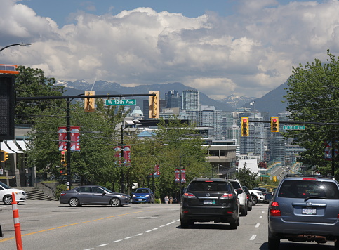 Vancouver, Canada - July 1, 2022: Looking north through tree-lined Cambie Village to the Cambie Bridge and downtown district in the background. Summer afternoon with clouds.