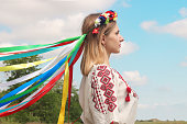 Portrait of Ukrainian young girl in profile view in national costume with wreath on her head on background of field with poppies and blue sky . Ethnic Ukrainian costume. Patriotic themes