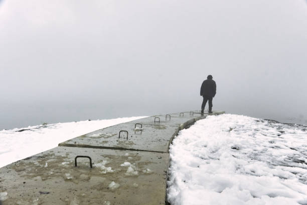 Side view of unrecognizable male standing on concrete quay near pond located in winter